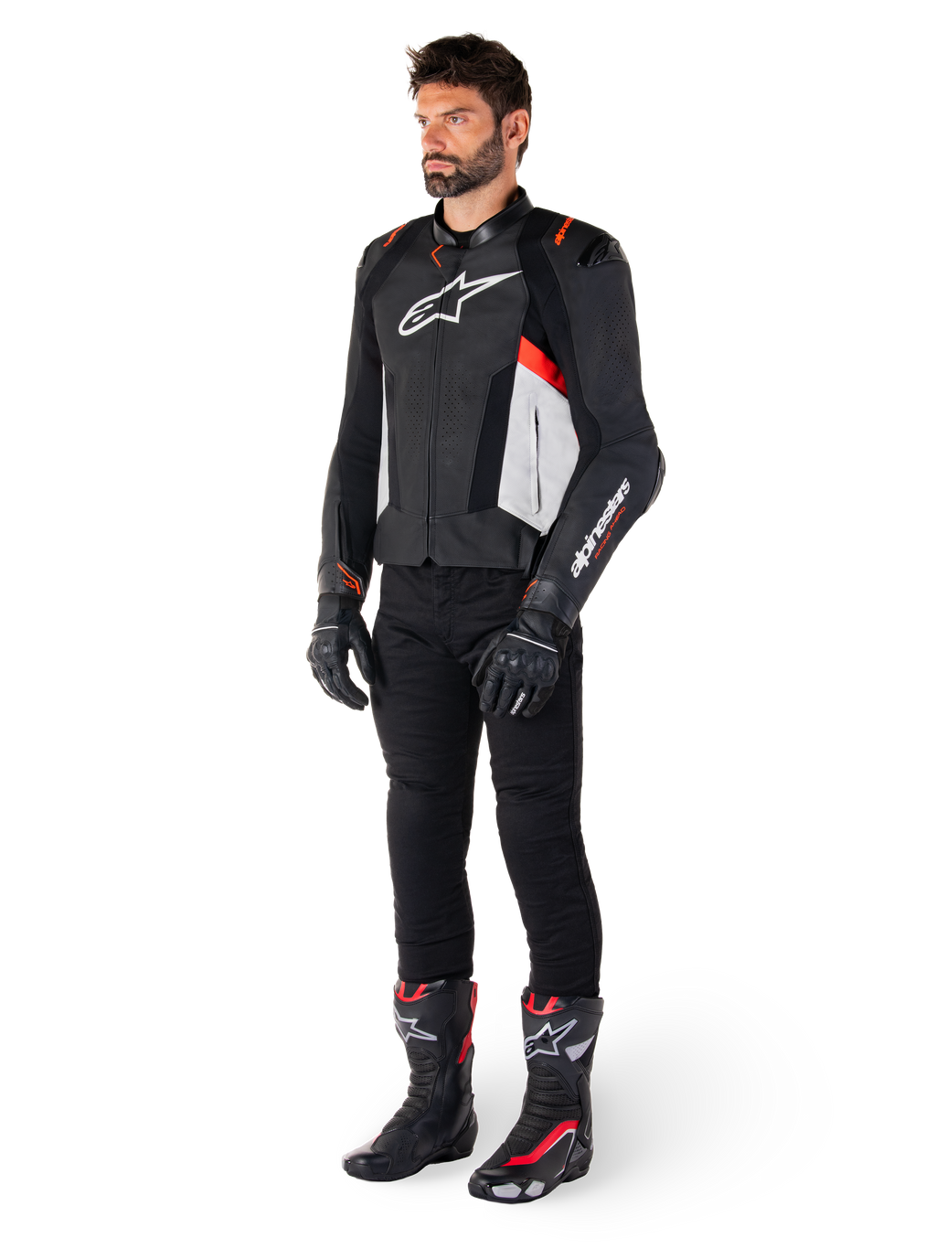 Modelo masculino con la chaqueta de cuero Alpinestars Missile V3 en negro, blanco y rojo flúor, combinada con pantalones, guantes y botas de motociclista negros, con confección en cuero bovino premium, logotipos destacados de Alpinestars y estética deportiva de competición profesional