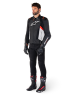 Modelo masculino con la chaqueta de cuero Alpinestars Missile V3 en negro, blanco y rojo flúor, combinada con pantalones, guantes y botas de motociclista negros, con confección en cuero bovino premium, logotipos destacados de Alpinestars y estética deportiva de competición profesional
