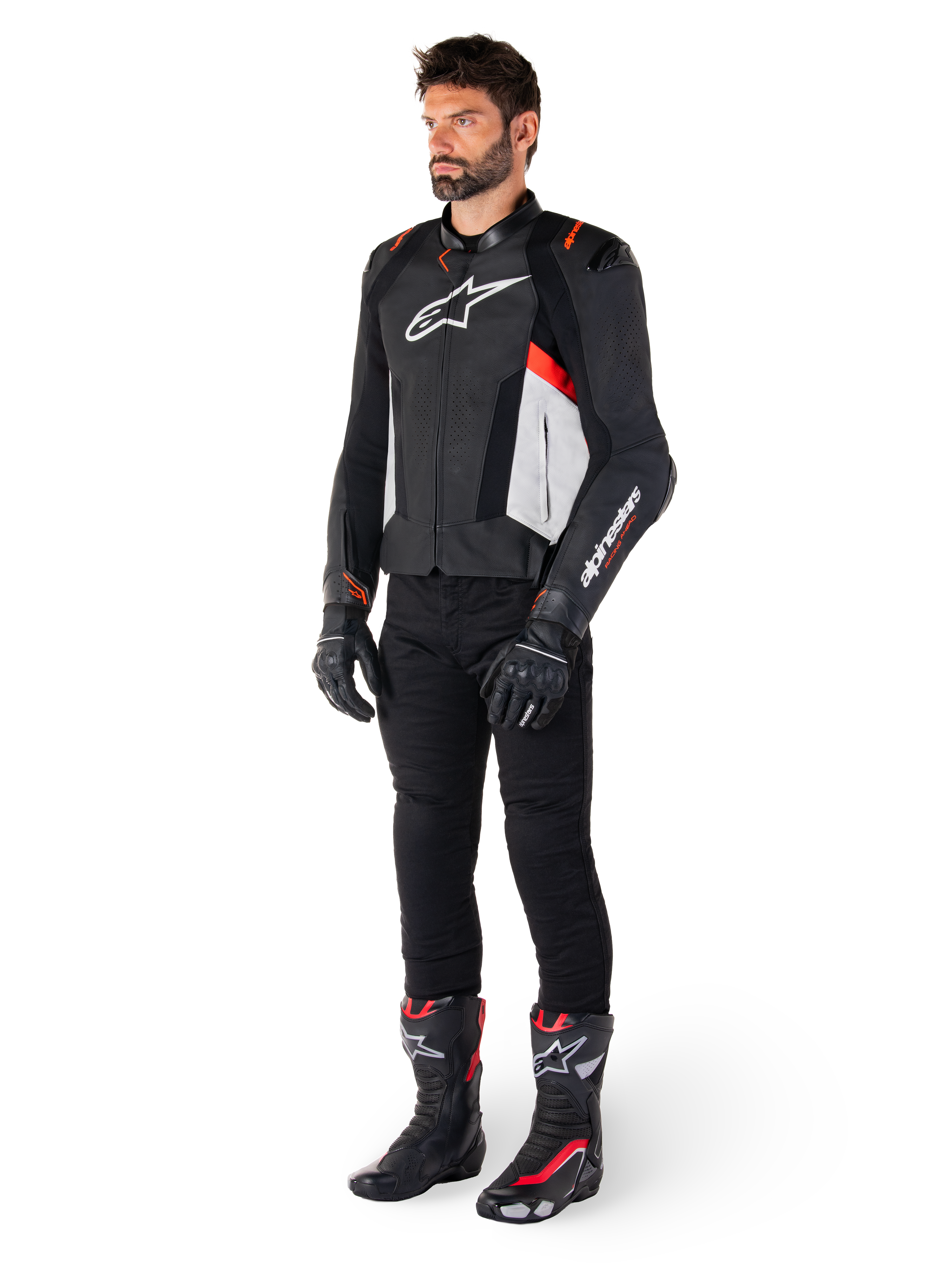 Modelo masculino con la chaqueta de cuero Alpinestars Missile V3 en negro, blanco y rojo flúor, combinada con pantalones, guantes y botas de motociclista negros, con confección en cuero bovino premium, logotipos destacados de Alpinestars y estética deportiva de competición profesional