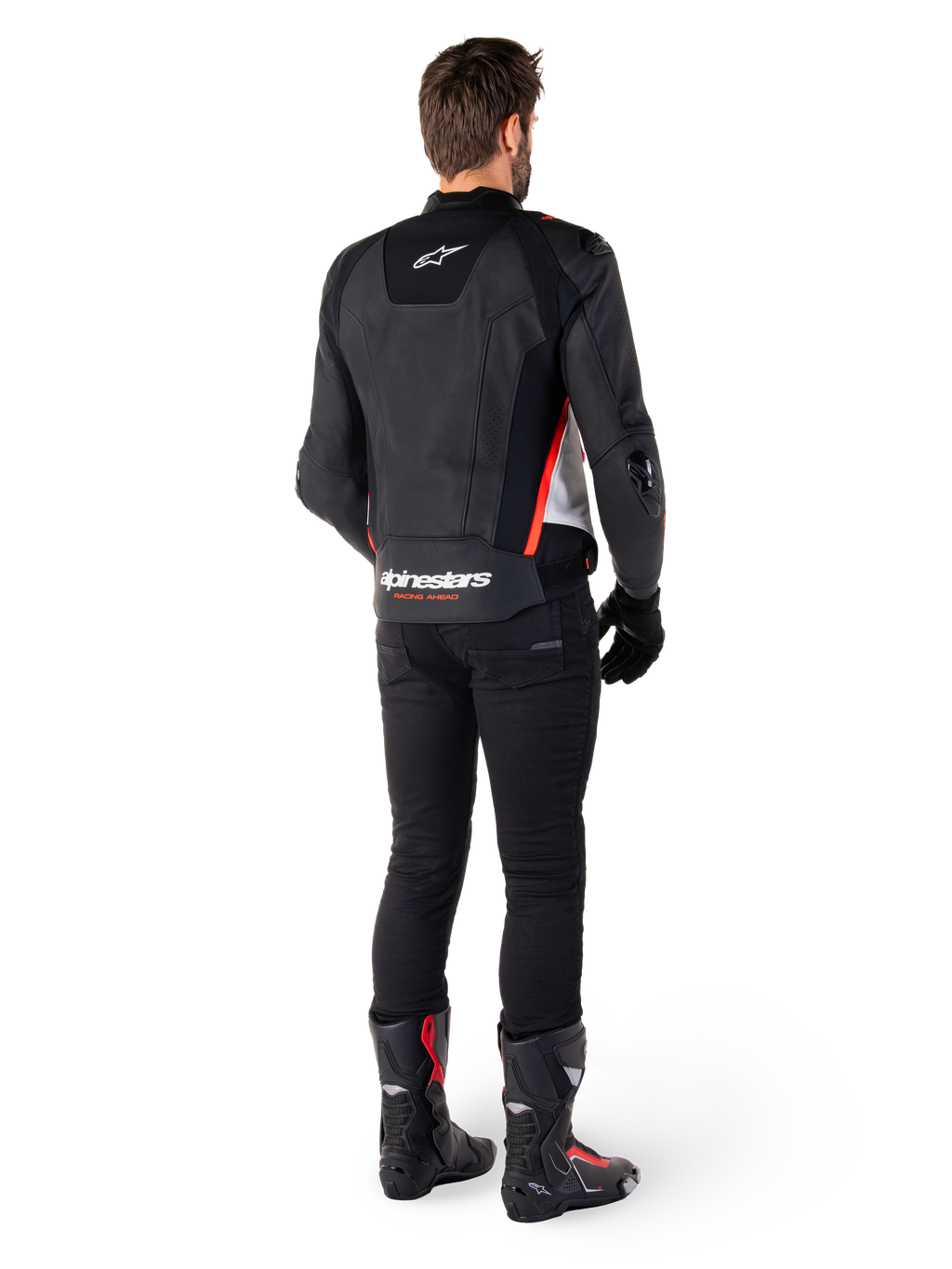 Chaqueta de cuero Alpinestars Missile V3 en Negro Blanco Rojo Fluo, vista trasera en un piloto masculino, con logotipos de Alpinestars en la parte superior e inferior de la espalda, combinada con pantalones negros y botas de moto, chaqueta deportiva de cuero inspirada en la competición