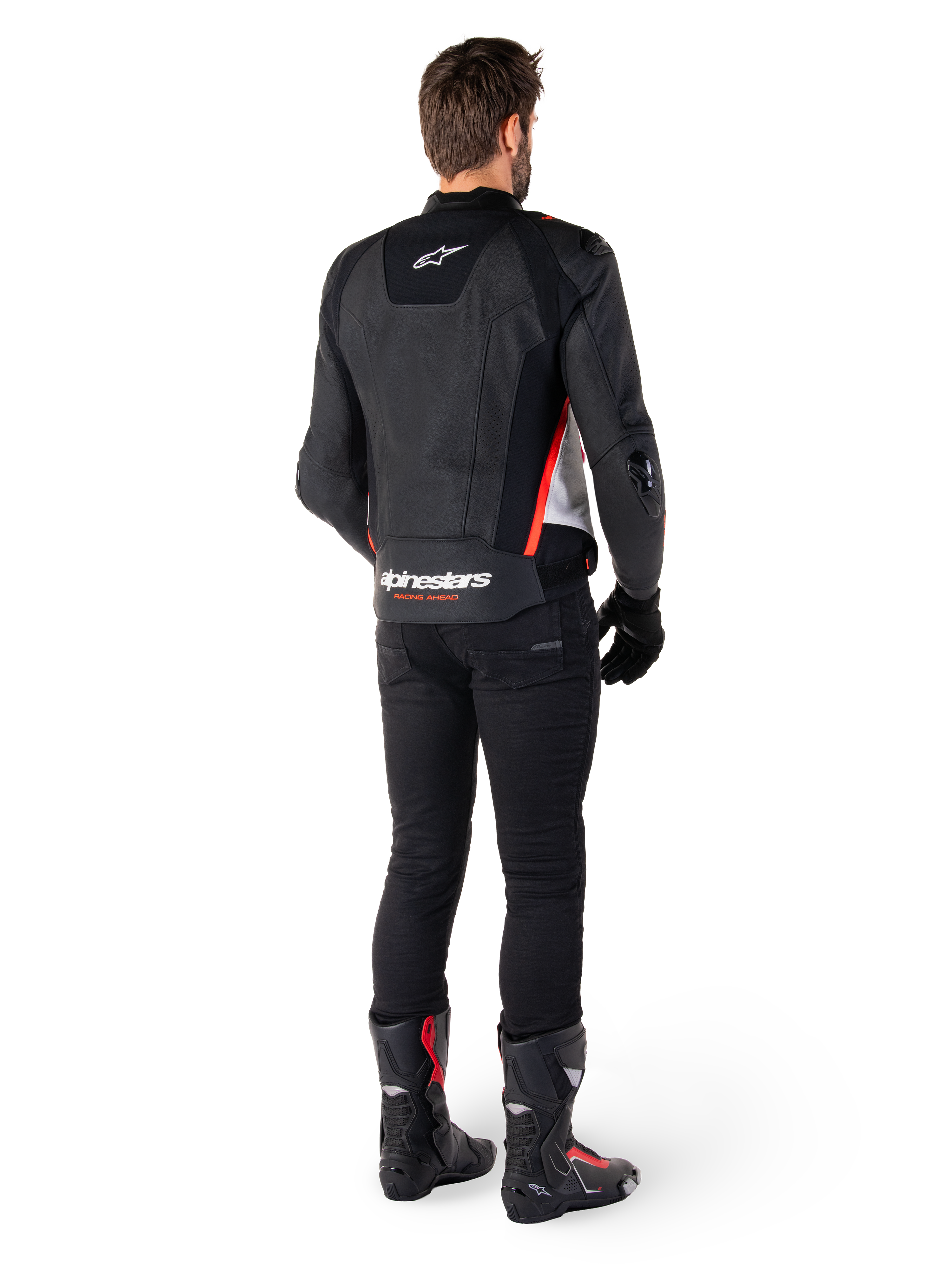 Chaqueta de cuero Alpinestars Missile V3 en Negro Blanco Rojo Fluo, vista trasera en un piloto masculino, con logotipos de Alpinestars en la parte superior e inferior de la espalda, combinada con pantalones negros y botas de moto, chaqueta deportiva de cuero inspirada en la competición