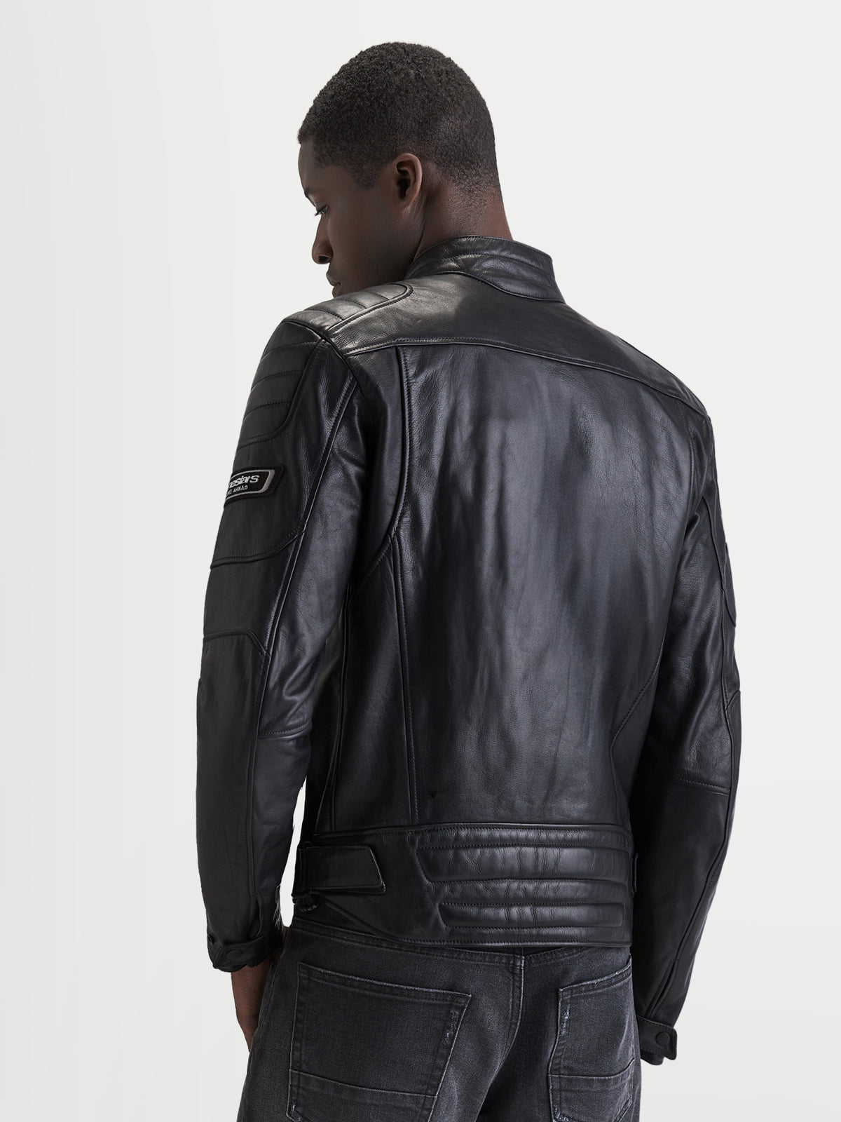 Alpinestars Revern Chaqueta de cuero, chaqueta de moto de cuero negra para hombre, vista trasera en un modelo que muestra la construcción de cuero bovino flor envejecido, cuello de estilo clásico y detalles de la marca