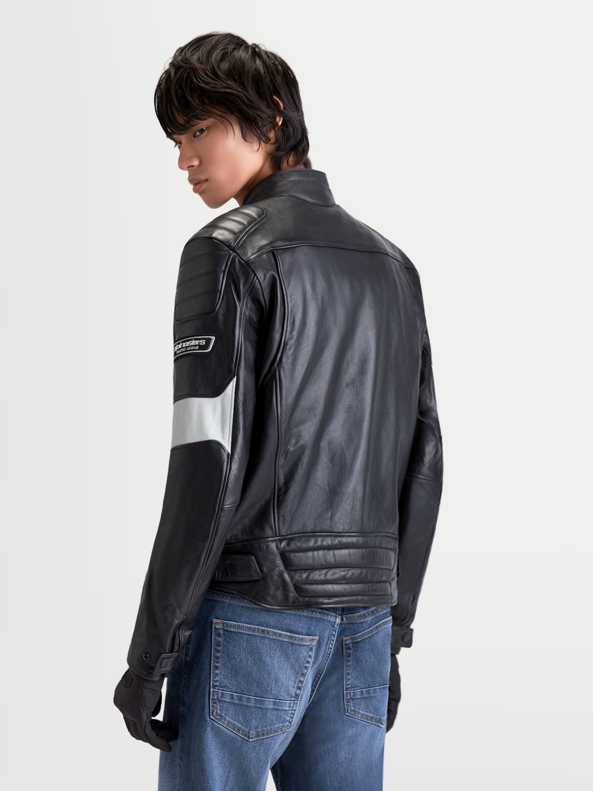 Alpinestars Revern Leather Jacket, men's urban motorcycle leather jacket in black and metal gray, rear three-quarter view on a model wearing jeans, showing distressed bovine leather construction and heritage styling.