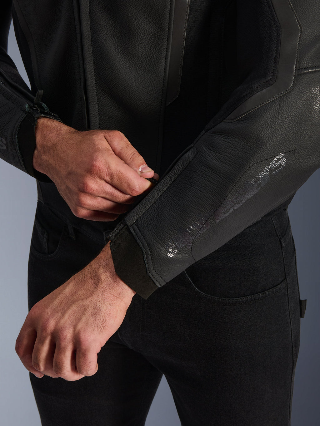 Chaqueta de cuero Alpinestars GP Force V2, negra, primer plano del puño ergonómico de la manga, persona ajustando el cierre de la muñeca, construcción en cuero bovino premium con detalles técnicos para conducción deportiva de motocicletas