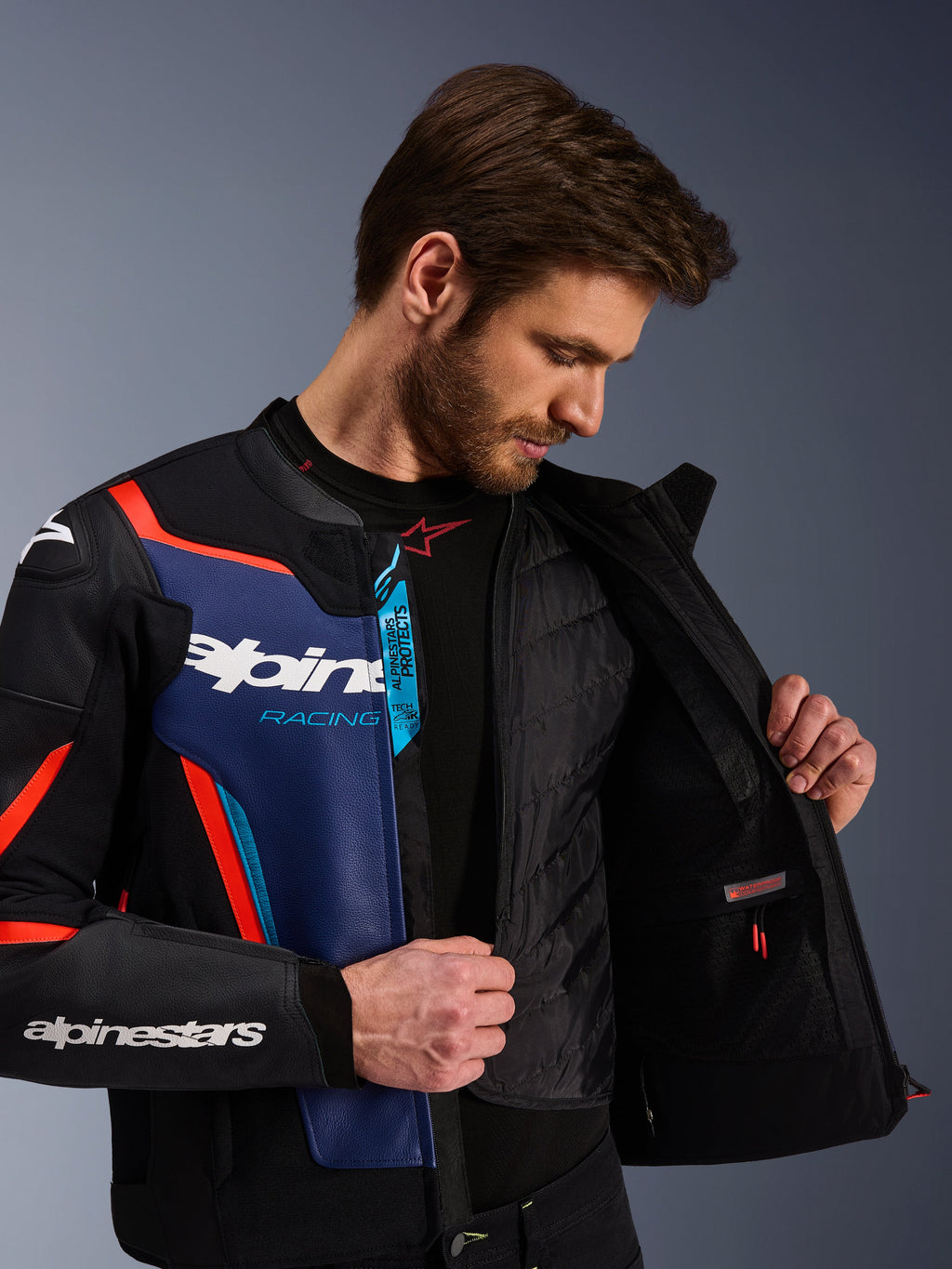Chaqueta de cuero Alpinestars GP Force V2 en negro, azul y rojo flúor, vista de cerca que muestra el chaleco térmico interno desmontable y el bolsillo impermeable, cuero bovino premium con marca Tech-Air Ready, equipamiento de moto deportivo.