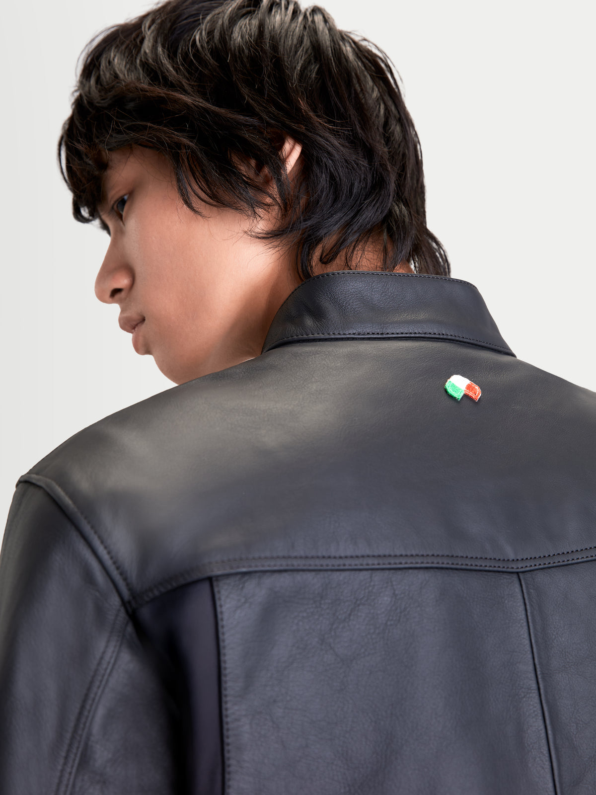 Alpinestars Maver X, chaqueta de moto de cuero urbana para hombre en color negro, vista trasera en primer plano que muestra la construcción de cuero bovino premium, cuello estilo motero y detalle de la bandera italiana en modelo