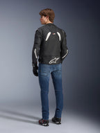 Chaqueta de cuero Alpinestars GP Plus R V4 Rideknit en negro y blanco, vista posterior en un modelo, con la marca Alpinestars en blanco en las mangas y un gran logotipo de estrella en la parte inferior de la espalda, usada con vaqueros azules y calzado de moto negro, equipamiento técnico de motociclismo.