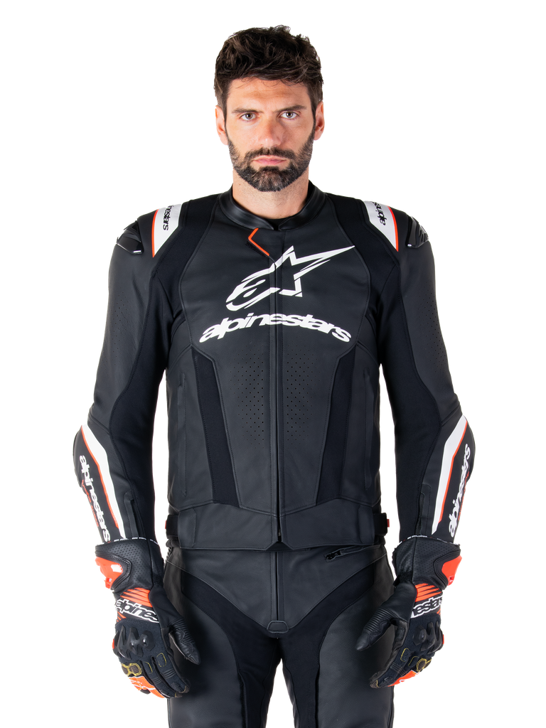 Chaqueta de cuero Alpinestars Missile V3 Ignition, negra con detalles en blanco y rojo, lucida por un modelo masculino con guantes y pantalones de carreras a juego, chaqueta deportiva de motociclismo derivada de MotoGP con logotipos llamativos