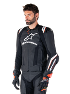 Modelo masculino vistiendo la chaqueta de cuero Alpinestars Missile V3 Ignition, negra con detalles en blanco y naranja, con logotipos blancos prominentes, secciones de cuero perforado y protecciones en los hombros, combinada con guantes de carreras para un look deportivo de competición