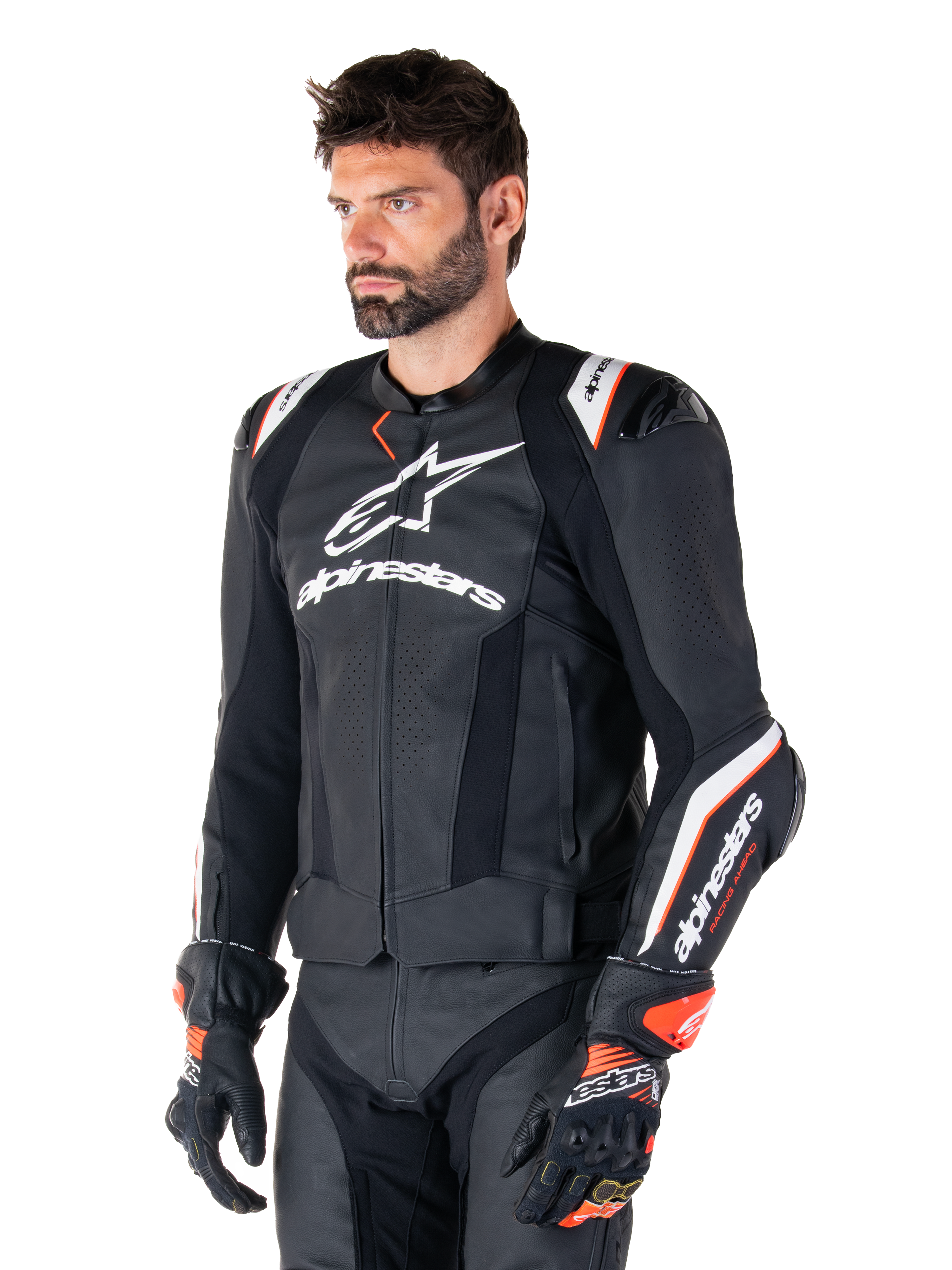 Modelo masculino vistiendo la chaqueta de cuero Alpinestars Missile V3 Ignition, negra con detalles en blanco y naranja, con logotipos blancos prominentes, secciones de cuero perforado y protecciones en los hombros, combinada con guantes de carreras para un look deportivo de competición