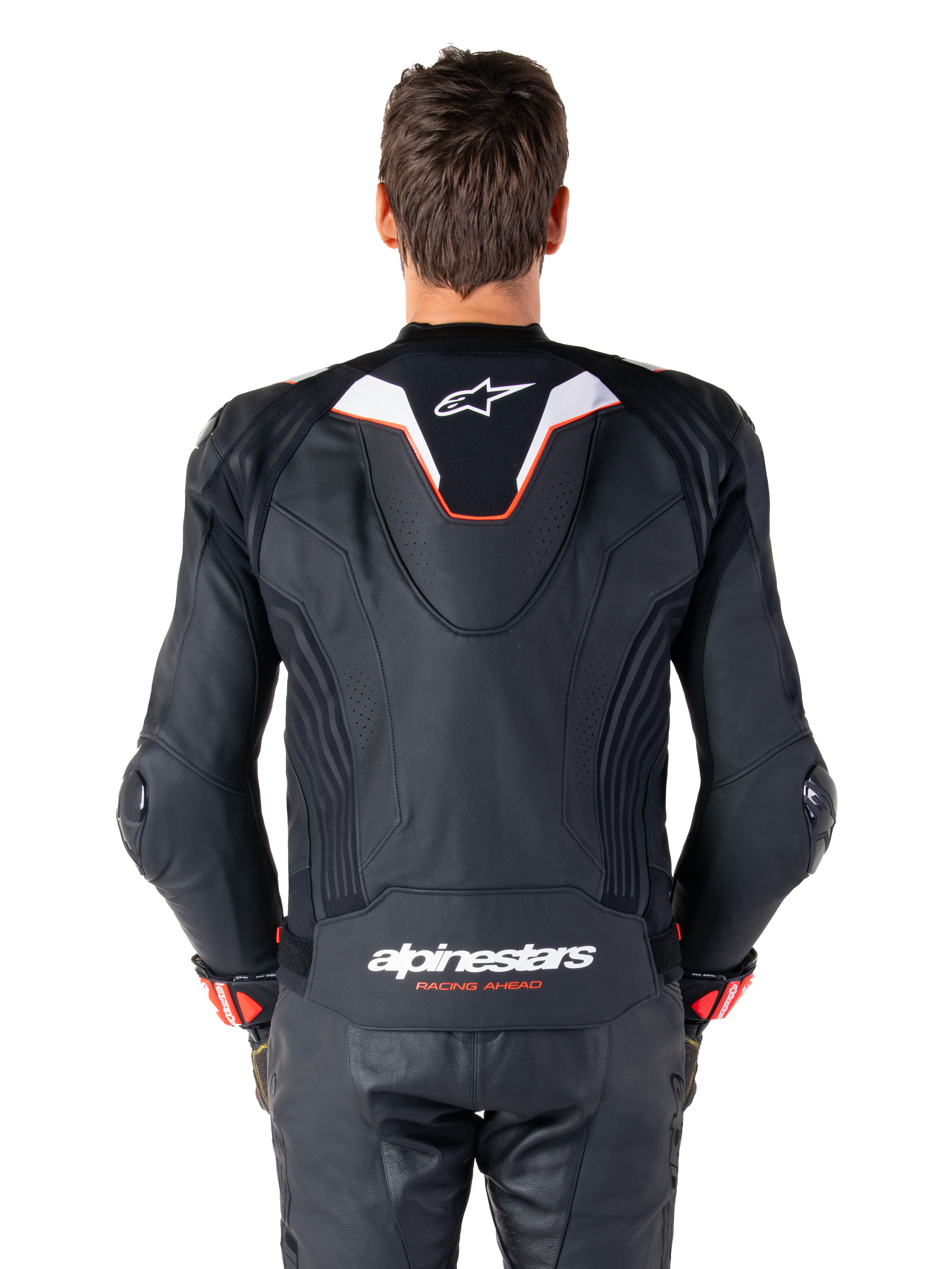Vista posterior de un piloto con la chaqueta de cuero Alpinestars Missile V3 Ignition, de cuero negro con detalles en blanco y rojo, con una joroba aerodinámica deportiva delgada con logo blanco y la marca 'alpinestars RACING AHEAD' en la parte inferior de la espalda, combinada con pantalones de carreras y guantes de cuero negro a juego.