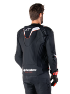 Chaqueta de cuero Alpinestars Missile V3 Ignition, vista trasera, negra con detalles en blanco y rojo, con joroba aerodinámica deportiva y logotipos de Alpinestars, usada con pantalones de cuero a juego y guantes de carreras