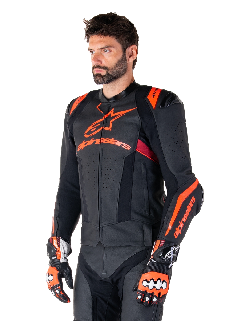 Chaqueta de cuero Alpinestars Missile V3 Ignition, negra con detalles en rojo flúor y rojo oscuro, vestida por un modelo masculino con guantes de carreras y pantalones de cuero a juego, con logotipos llamativos de Alpinestars, paneles de cuero perforado y protectores externos en los hombros, equipo profesional de carreras de motos
