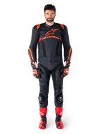 Modelo masculino con la chaqueta de cuero Alpinestars Missile V3 Ignition en color negro, rojo flúor y rojo oscuro, equipamiento completo de competición para moto con pantalones de cuero a juego, guantes y botas de carreras, marca Alpinestars destacada en el pecho, pose frontal, atuendo profesional de conducción deportiva