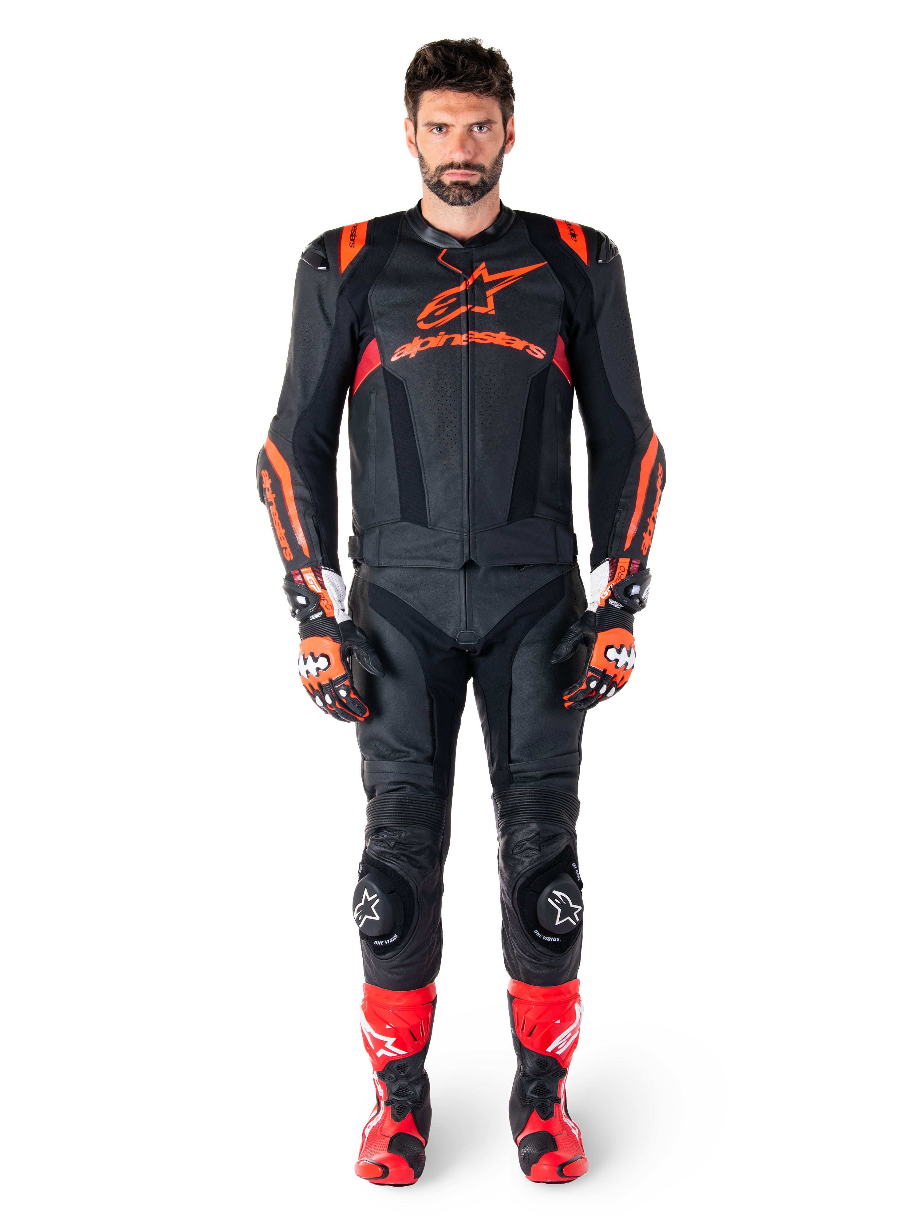 Modelo masculino con la chaqueta de cuero Alpinestars Missile V3 Ignition en color negro, rojo flúor y rojo oscuro, equipamiento completo de competición para moto con pantalones de cuero a juego, guantes y botas de carreras, marca Alpinestars destacada en el pecho, pose frontal, atuendo profesional de conducción deportiva
