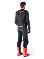 Alpinestars Missile V3 Ignition Leather Jacket, chaqueta de moto deportiva de competición, negro y rojo flúor, vista trasera de un piloto con equipación de carreras completa con pantalones de cuero, guantes y botas rojas a juego, con joroba aerodinámica deportiva y logotipo llamativo en la parte baja de la espalda.