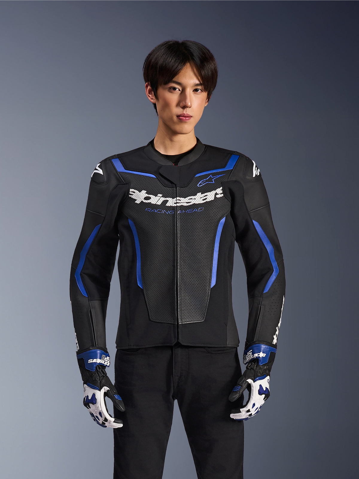 Chaqueta de cuero Alpinestars GP Force V2 Airflow, Negro Azul Metálico, chaqueta de moto con cuero perforado y detalles en azul, usada por un modelo con guantes de carreras a juego y pantalones negros, equipamiento profesional para conducción deportiva