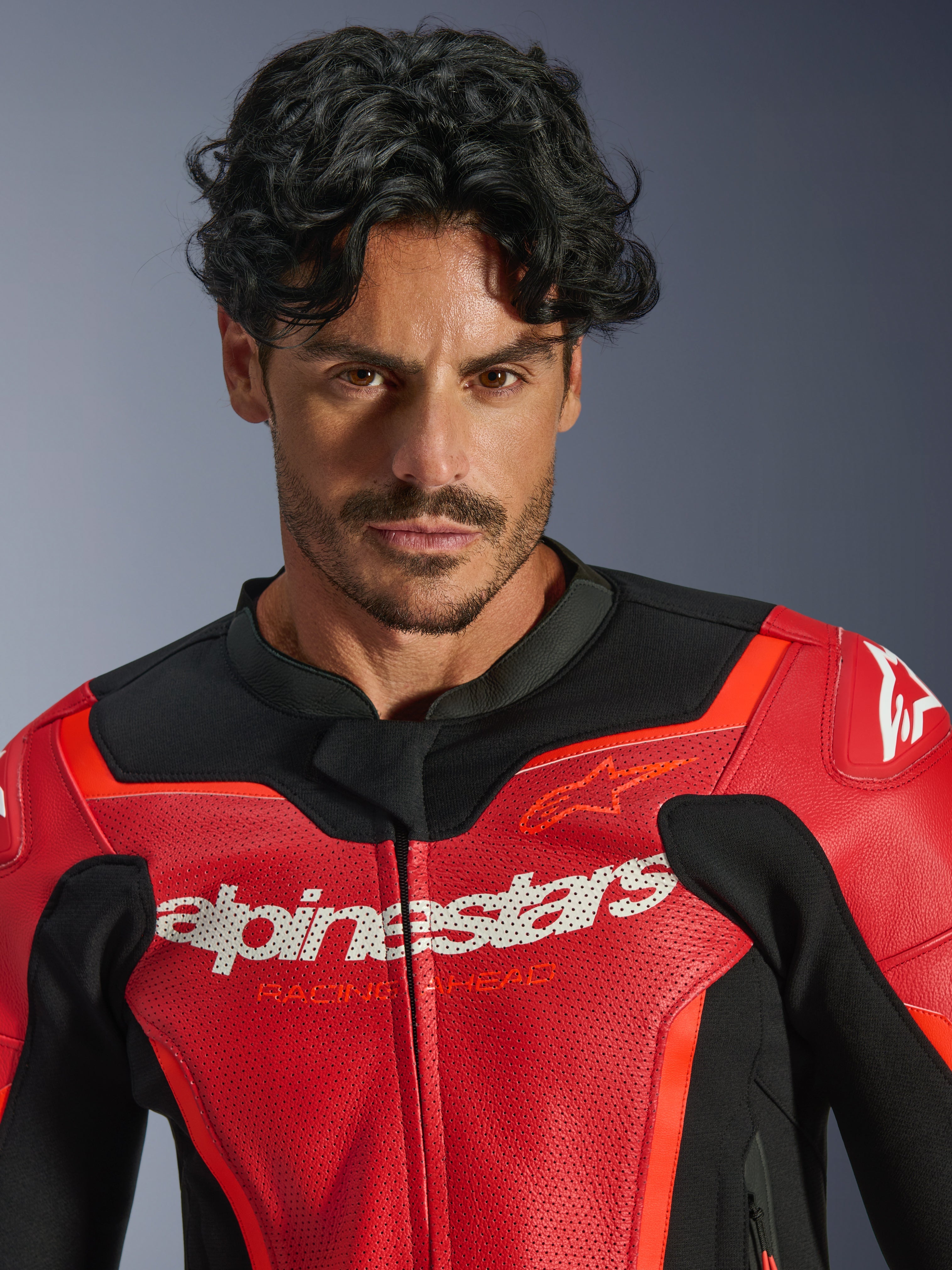 Chaqueta de cuero Alpinestars GP Force V2 Air, rojo y rojo flúor, usada por un modelo masculino, con logotipos blancos de Alpinestars y 'Racing Ahead' en el pecho, cuero perforado para el flujo de aire, equipamiento de moto de estilo deportivo