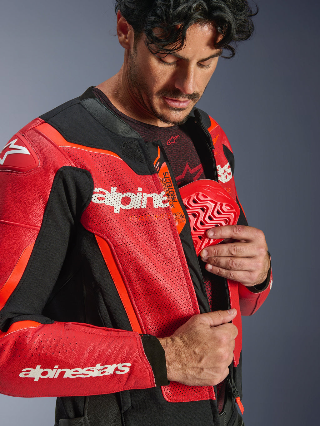 Chaqueta de cuero Alpinestars GP Force V2 Air, Rojo y Rojo Flúor, primer plano de un piloto insertando un protector de pecho rojo en el bolsillo interior, con cuero perforado y logotipo Tech-Air Ready, protección deportiva premium para motociclismo.