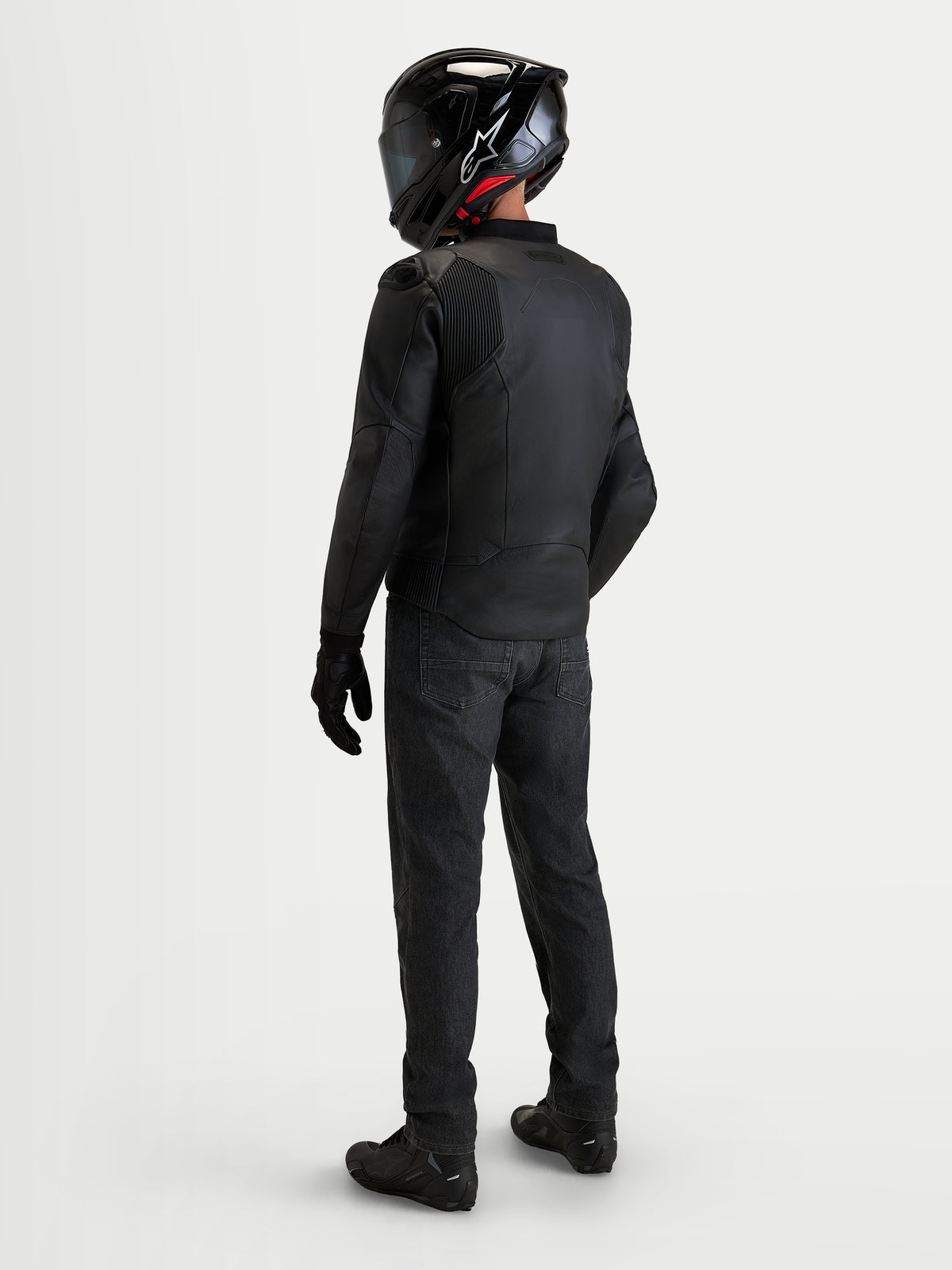 Alpinestars Caliber V2, chaqueta de moto de cuero para hombre, color negro, vista trasera de un piloto con casco y vaqueros