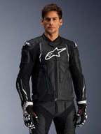 Chaqueta de cuero Alpinestars Dusk, negra y blanca, chaqueta de moto de cuero con áreas de protección acolchadas y logotipos blancos, combinada con guantes de carreras negros y blancos con detalles rojos, equipamiento profesional para conducción deportiva