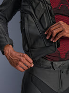 Chaqueta de cuero Alpinestars Dusk, negra, primer plano de la cremallera de conexión de la cintura uniéndose a unos pantalones de moto de cuero, con una capa base de patrón rojo y negro, construcción de cuero duradero para conducción en carretera.