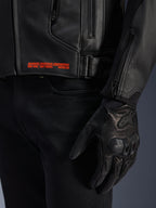 Alpinestars GP Plus V4 Leather Jacket, chaqueta de cuero negra, primer plano del detalle lateral con texto de marca naranja 'ADVANCED RACEWEAR ENGINEERING', hebilla ajustable y guante de cuero negro, ropa deportiva para motocicleta
