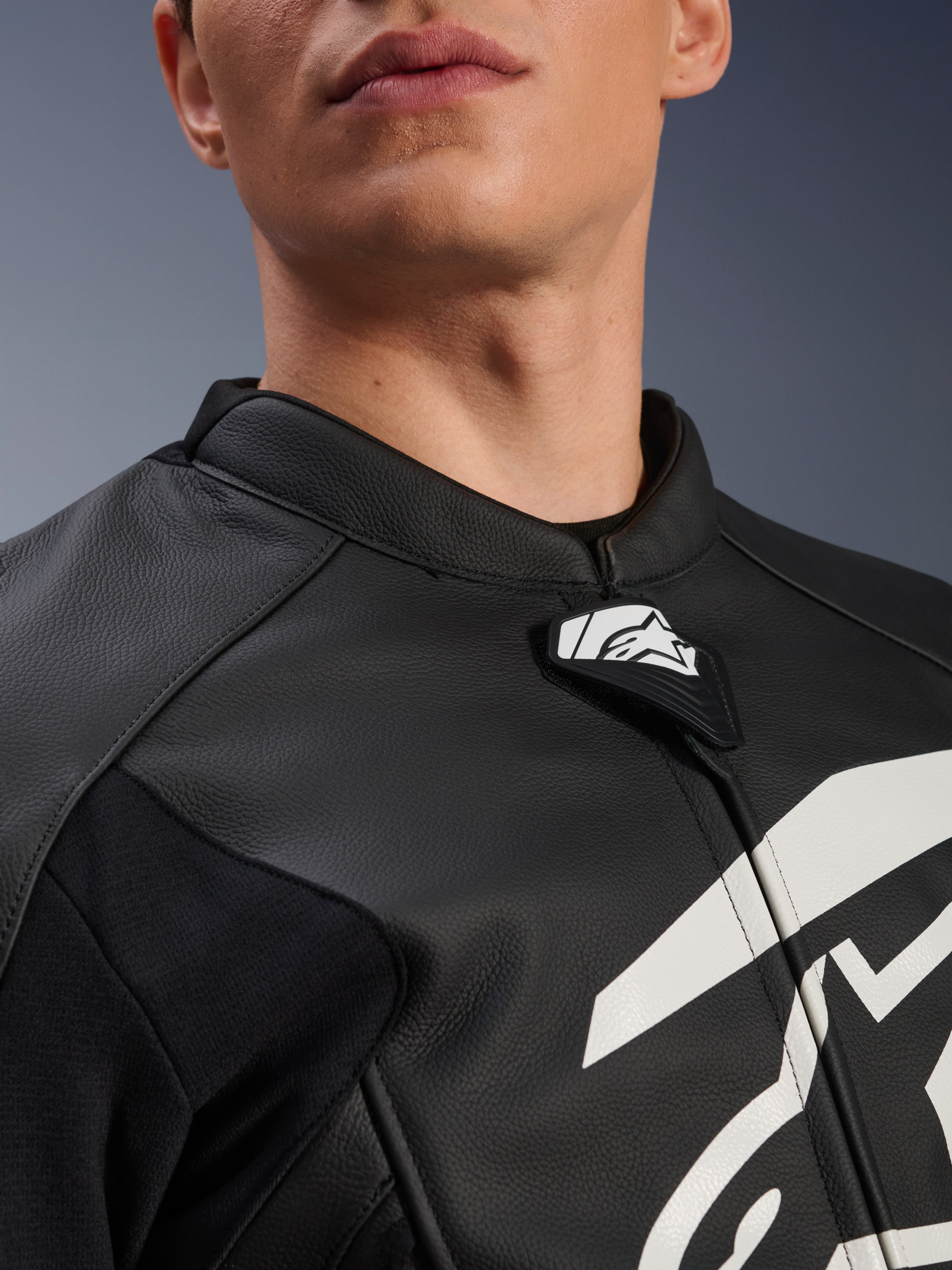 Alpinestars GP Plus V4 Leather Jacket, chaqueta deportiva de moto, negra y blanca, primer plano del cuello de cuero texturizado y la lengüeta con el logo de Alpinestars, gráfico blanco en el pecho, diseño derivado de la competición