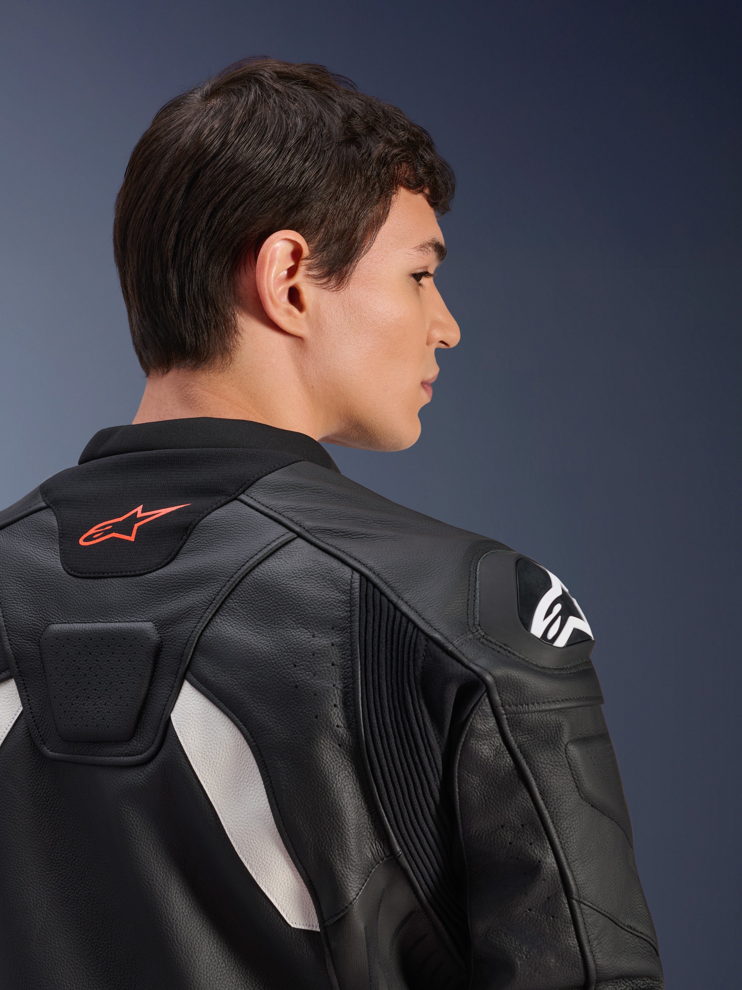 Chaqueta de cuero Alpinestars GP Plus V4, negro y blanco, vista trasera en primer plano de un modelo con la chaqueta puesta, con un logotipo rojo en el cuello, protectores de hombros blancos y confección de cuero duradero con paneles elásticos