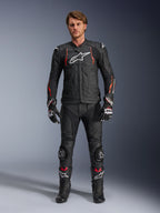 Piloto con la chaqueta de cuero Alpinestars Dusk Airflow en Negro Rojo Fluo, con paneles de cuero perforado y logotipo blanco en el pecho, combinada con pantalones de cuero negros a juego, deslizaderas, guantes y botas de competición; equipamiento completo de carretera para moto.