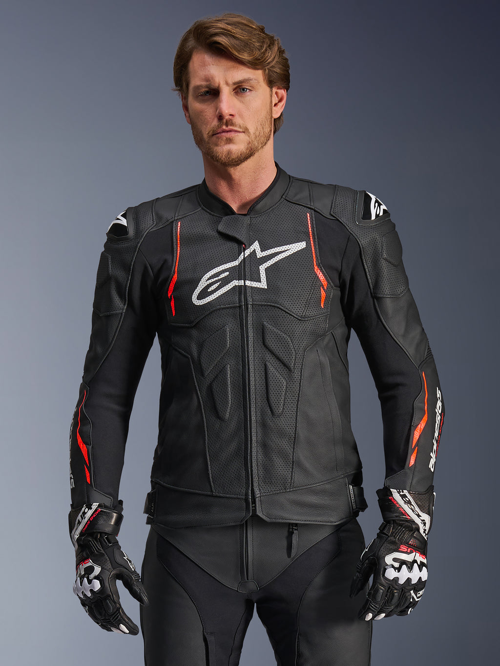 Alpinestars Dusk Airflow Leather Jacket, chaqueta de cuero para carreras de motos, negra con detalles en rojo flúor y blanco, con perforaciones extensas para ventilación, logotipo blanco en el pecho y deslizadores de hombros externos, vestida por un modelo con guantes de carreras a juego