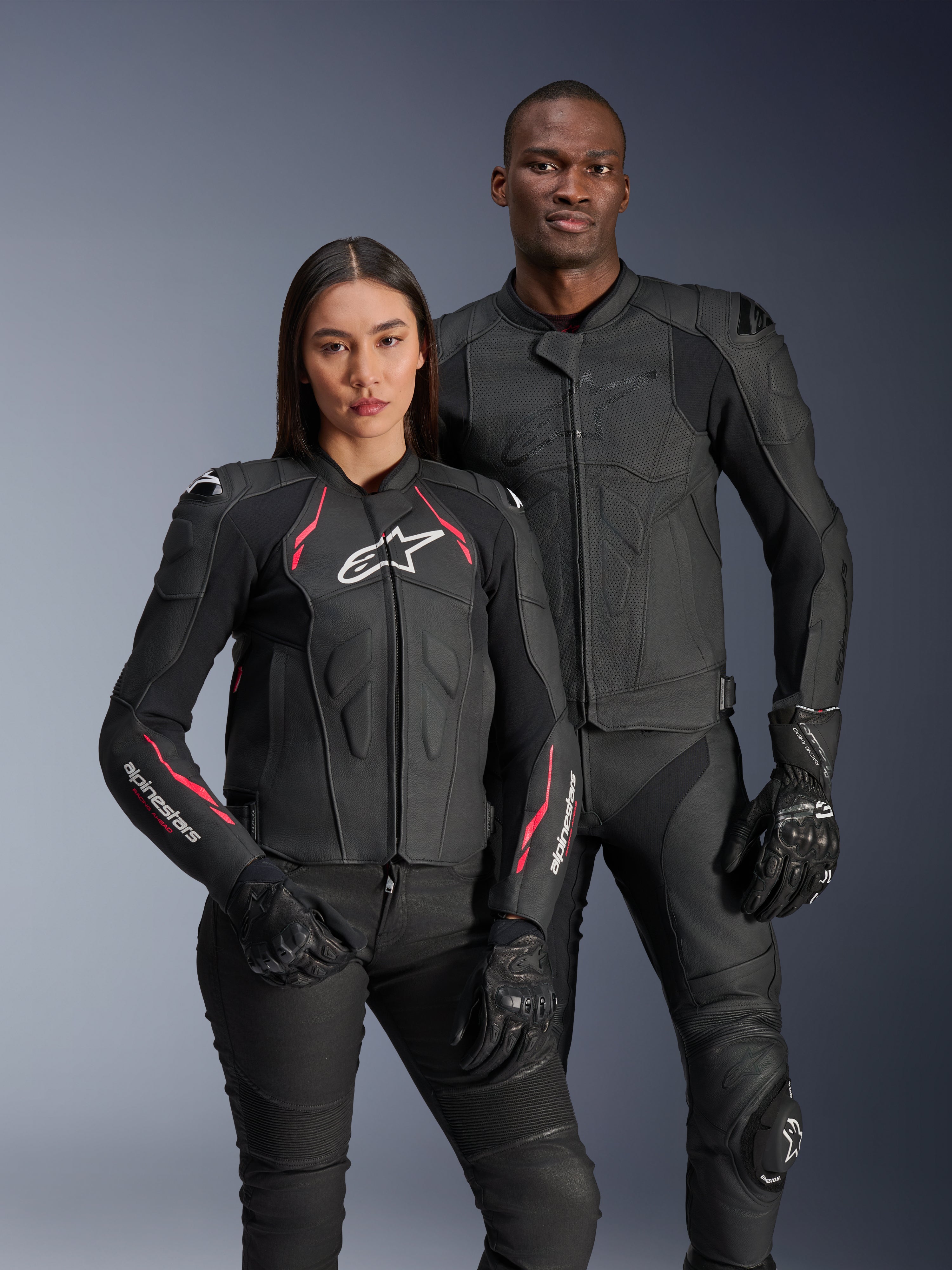 Chaquetas de cuero Alpinestars Dusk Airflow y Stella Dusk, pilotos hombre y mujer con chaquetas de cuero negro para motociclismo, la chaqueta de hombre cuenta con cuero perforado para ventilación, la chaqueta de mujer tiene detalles en rojo y logotipos blancos, coordinado con pantalones y guantes de conducción negros, equipamiento de conducción deportiva de alto rendimiento