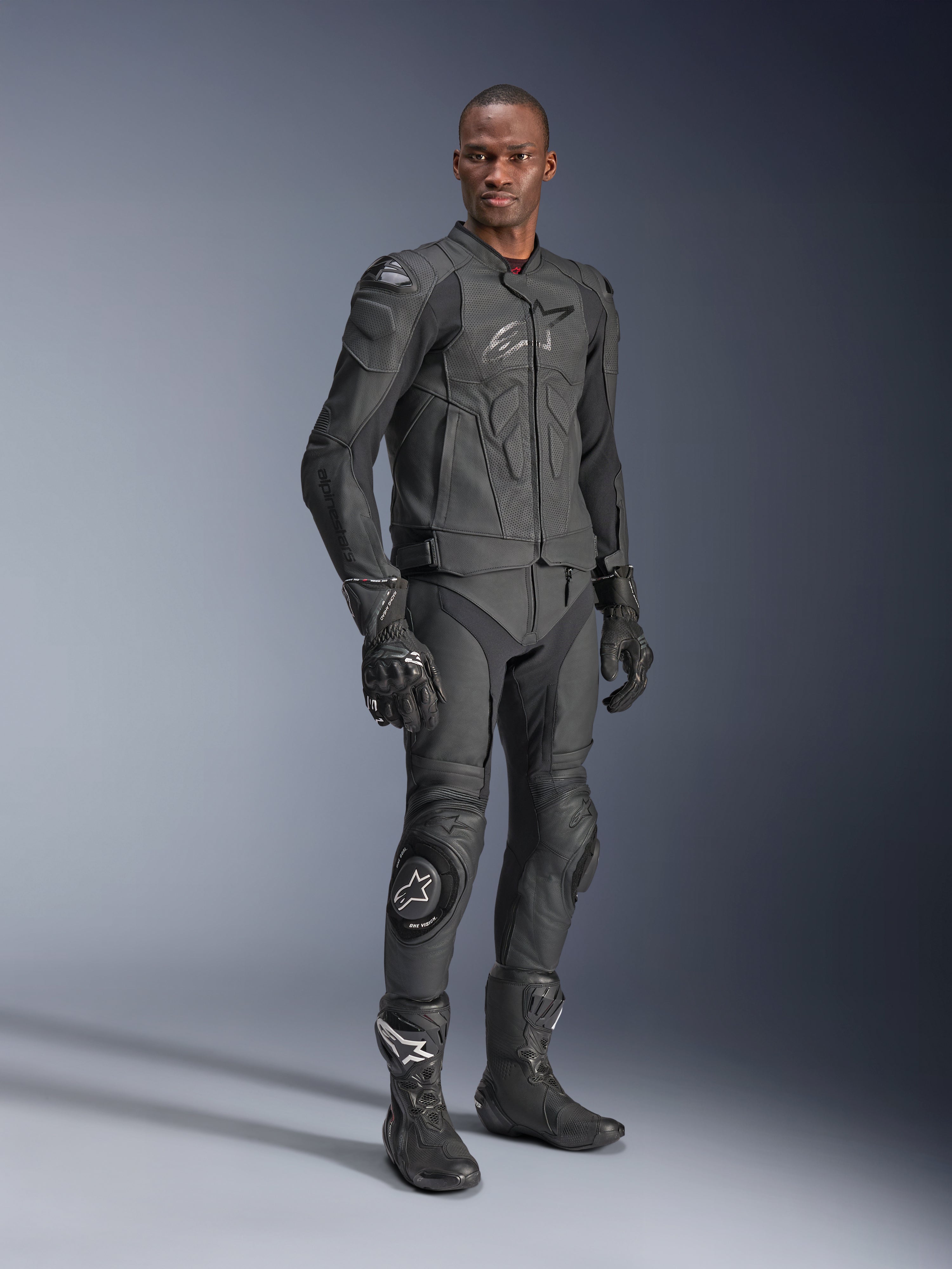 Chaqueta de cuero Alpinestars Dusk Airflow, Negro Negro, vestida por un piloto con equipamiento técnico completo que incluye pantalones de cuero, guantes y botas a juego, con paneles de cuero perforado para ventilación y armadura integrada para conducción deportiva de motocicletas.