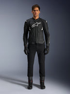 Chaqueta de cuero Alpinestars Dusk Airflow, negra y blanca, chaqueta de cuero para moto con paneles perforados para el flujo de aire, logotipo Astars blanco en el pecho, usada por un piloto masculino con pantalones negros, guantes y botas de conducción, toma de estudio profesional para equipamiento de moto deportiva.