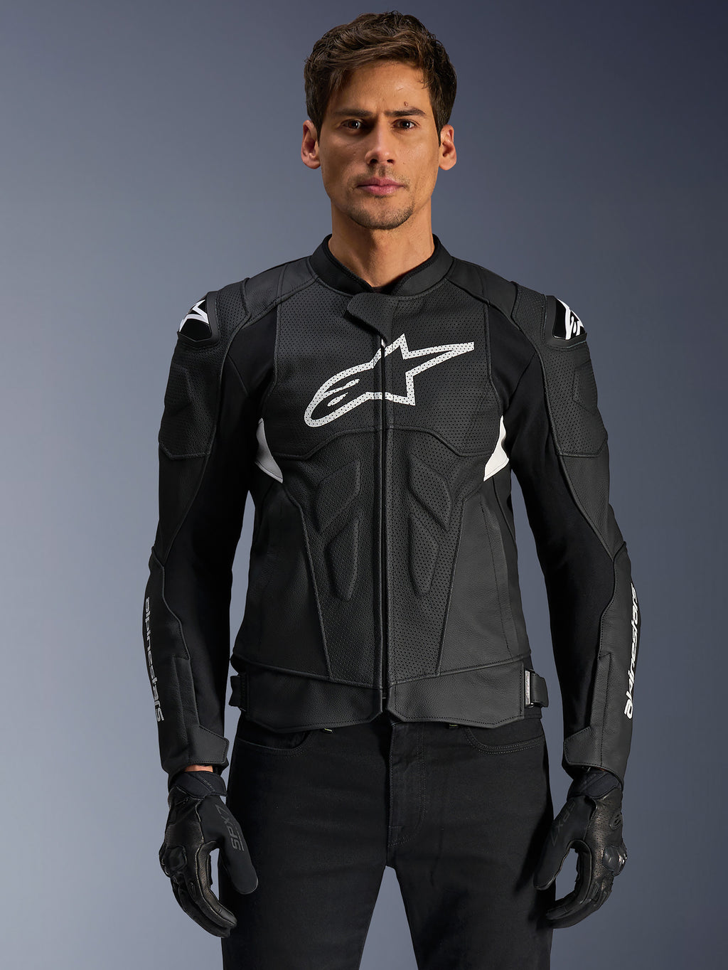 Alpinestars Dusk Airflow Leather Jacket, chaqueta de moto de cuero, negra y blanca, usada por un modelo, con paneles de cuero perforado para ventilación, un gran logotipo blanco en el pecho y deslizadores externos en los hombros.