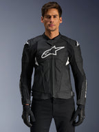 Alpinestars Dusk Airflow Leather Jacket, chaqueta de moto de cuero, negra y blanca, usada por un modelo, con paneles de cuero perforado para ventilación, un gran logotipo blanco en el pecho y deslizadores externos en los hombros.
