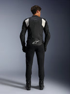 Chaqueta de cuero Alpinestars Dusk Airflow, en negro y blanco, vista trasera de un piloto con pantalones y botas negros, con cuero perforado para ventilación, paneles elásticos de acordeón blancos en los hombros y marca blanca en la parte baja de la espalda