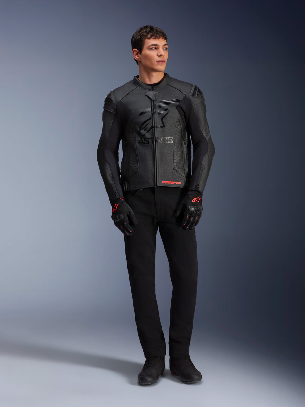 Chaqueta de cuero Alpinestars GP Plus R V4 Airflow, negra, lucida por un modelo masculino con guantes y pantalones negros a juego, con paneles de cuero perforado, gran logo de estrella tonal en el pecho y un ajuste deportivo estilizado para la conducción