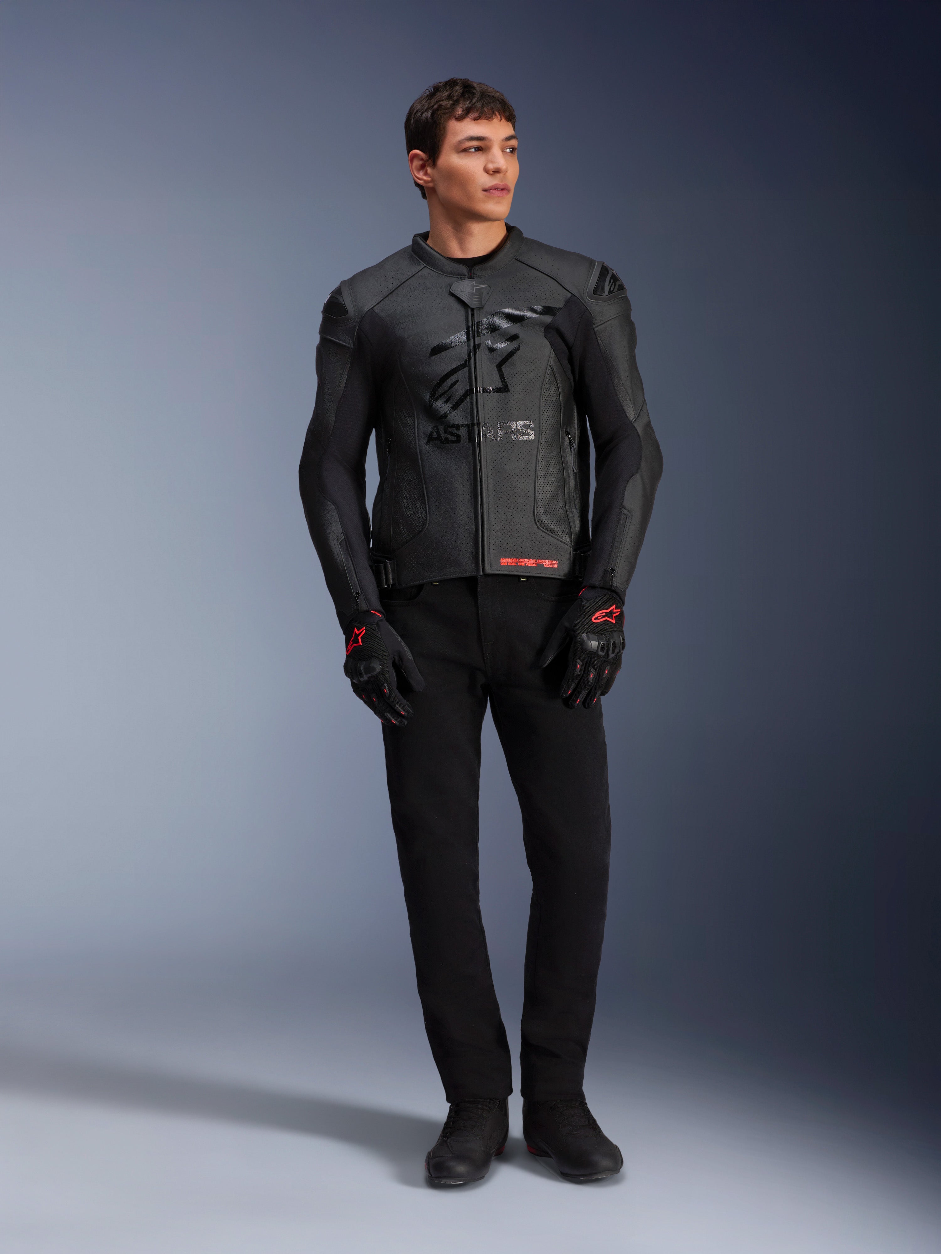 Chaqueta de cuero Alpinestars GP Plus R V4 Airflow, negra, lucida por un modelo masculino con guantes y pantalones negros a juego, con paneles de cuero perforado, gran logo de estrella tonal en el pecho y un ajuste deportivo estilizado para la conducción