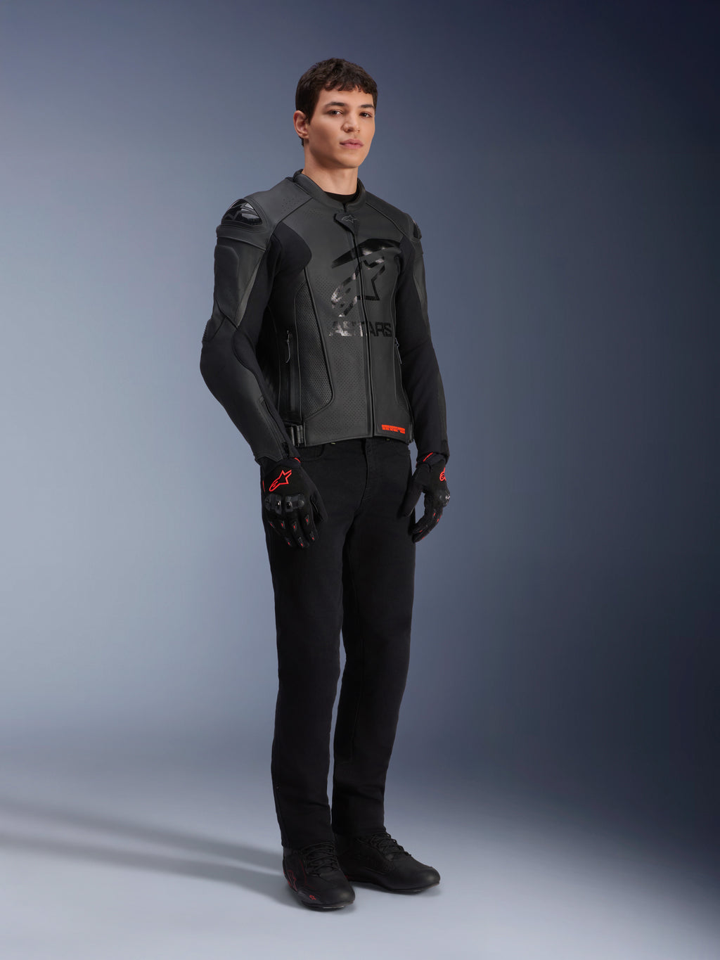 Chaqueta de cuero Alpinestars GP Plus R V4 Airflow, negra, usada por un modelo masculino con pantalones de montar negros y guantes con detalles rojos, con paneles de cuero perforado y deslizadores de hombro integrados, toma de estudio de cuerpo completo.