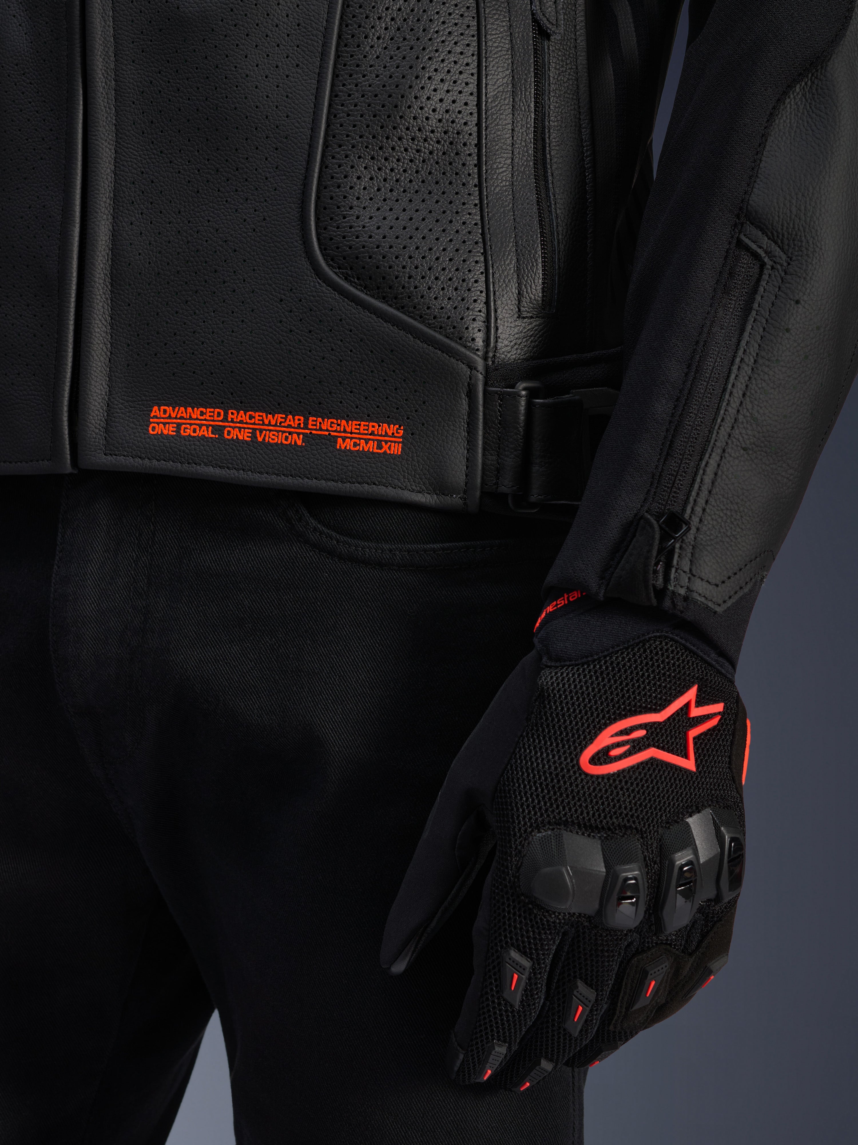 Chaqueta de cuero Alpinestars GP Plus R V4 Airflow, primer plano de cuero perforado negro con texto gráfico naranja, combinada con un guante de moto negro y naranja con el logotipo de Astars