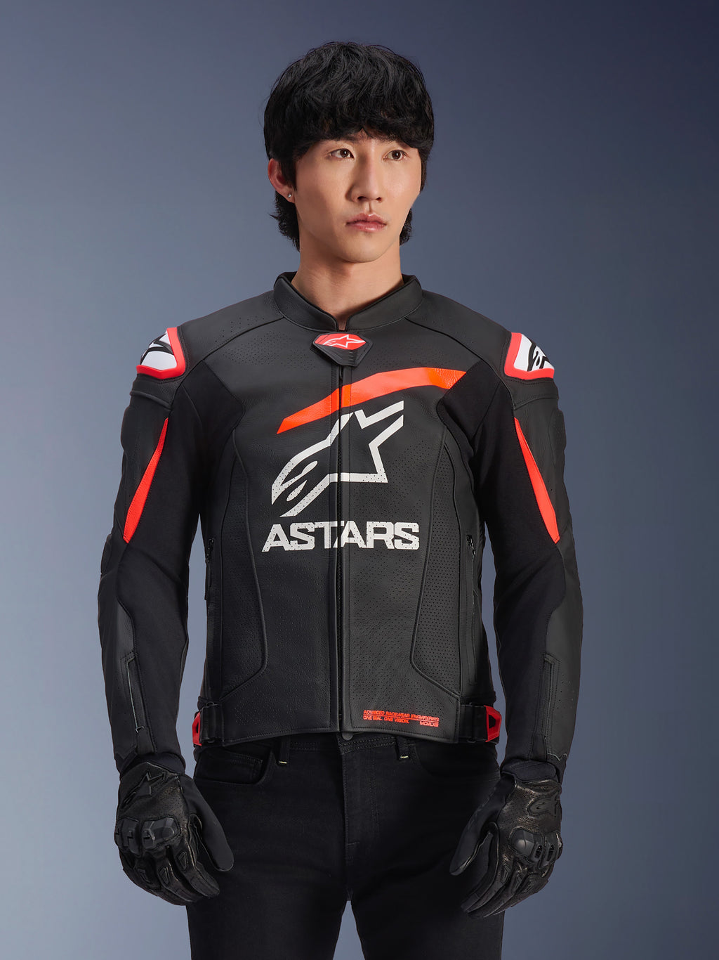 Chaqueta de cuero Alpinestars GP Plus R V4 Airflow en color negro con detalles en rojo fluo y blanco, vestida por un modelo, con construcción de cuero perforado, un gran logotipo ASTARS blanco en el pecho y protecciones de hombro integradas para carreras de motociclismo.