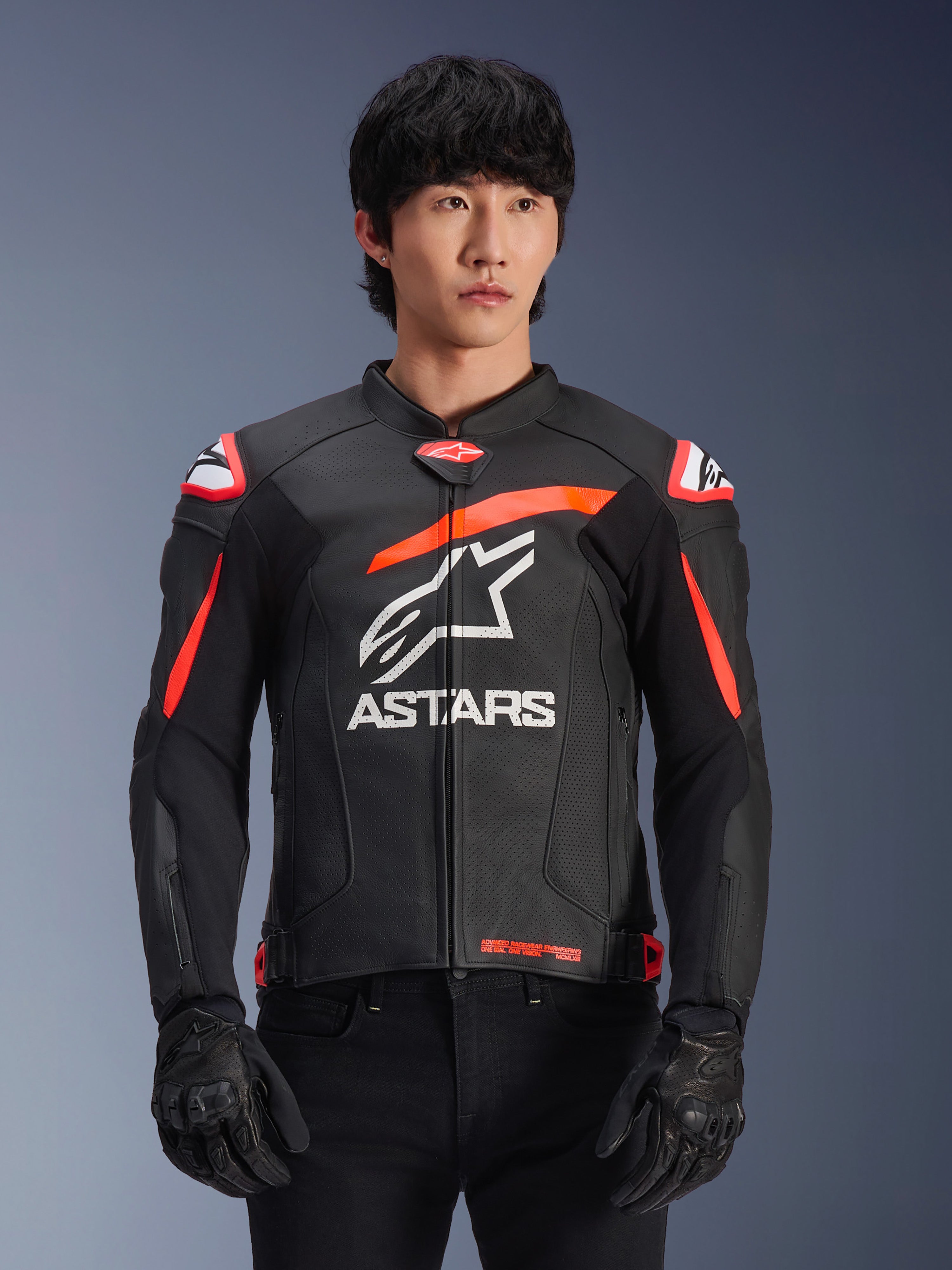 Chaqueta de cuero Alpinestars GP Plus R V4 Airflow en color negro con detalles en rojo fluo y blanco, vestida por un modelo, con construcción de cuero perforado, un gran logotipo ASTARS blanco en el pecho y protecciones de hombro integradas para carreras de motociclismo.