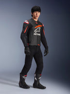 Piloto masculino con chaqueta de cuero Alpinestars GP Plus R V4 Airflow, negra con detalles en rojo flúor y blanco, con cuero perforado y logotipo ASTARS en el pecho, usada con pantalones de moto negros y botas de moto negras, equipamiento deportivo de alto rendimiento