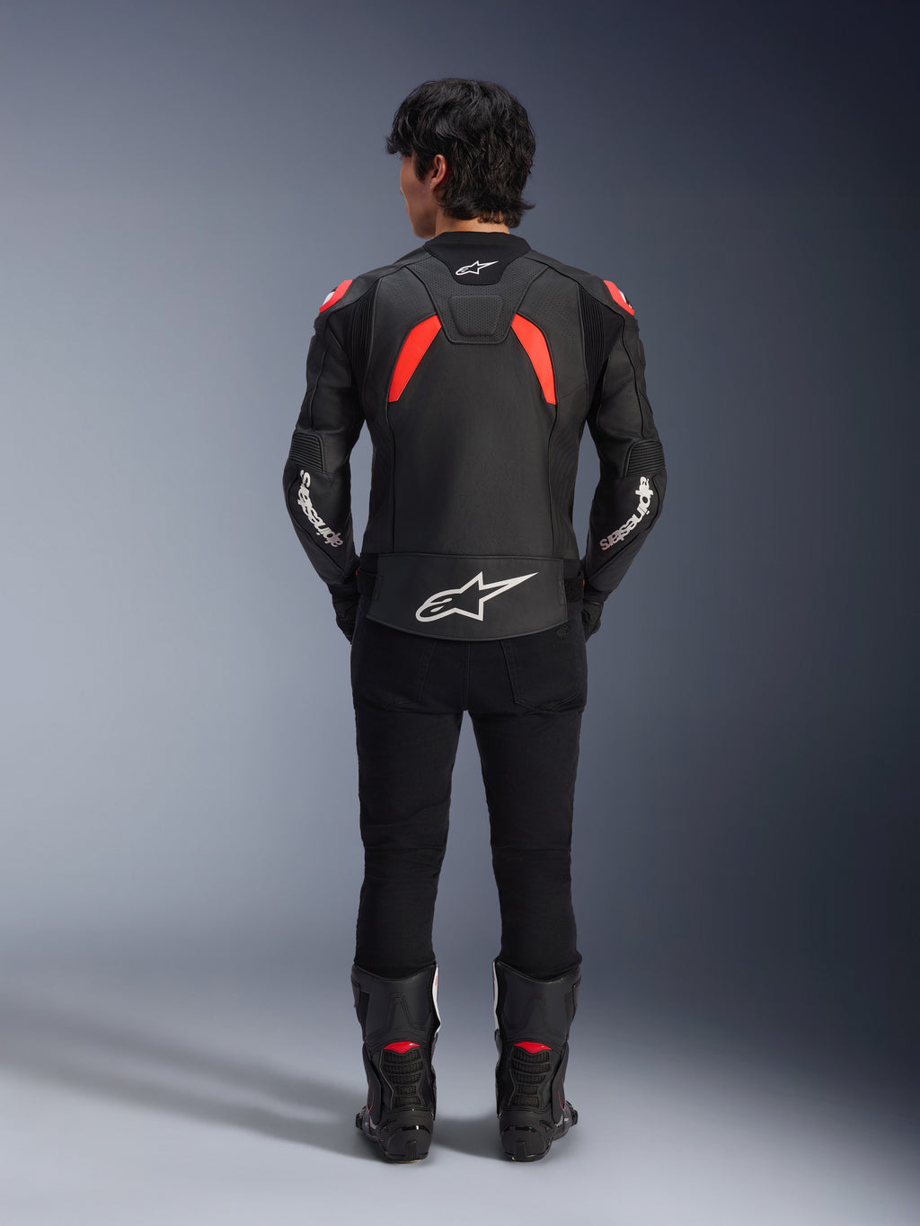 Chaqueta de cuero Alpinestars GP Plus R V4 Airflow, negro, rojo flúor y blanco, vista trasera en un modelo, con paneles de cuero perforados y logotipos blancos destacados, combinada con pantalones y botas de moto negros
