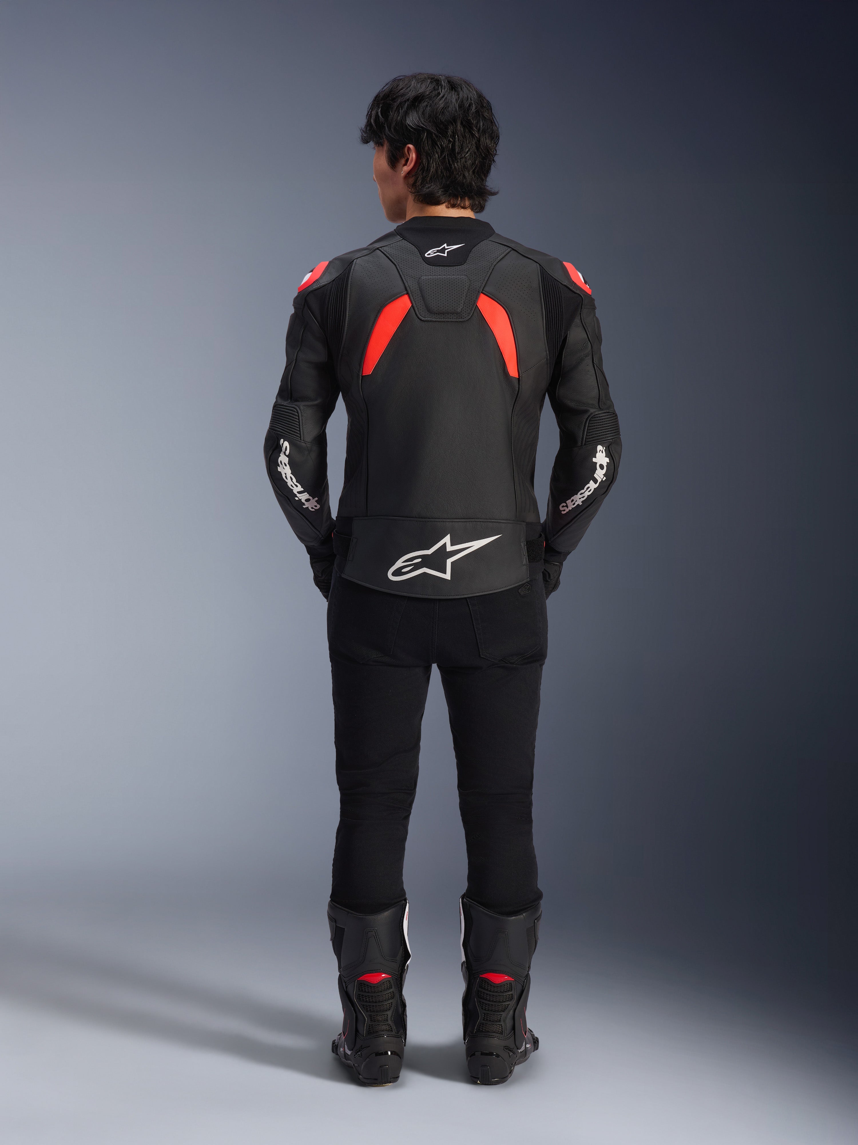 Chaqueta de cuero Alpinestars GP Plus R V4 Airflow, negro, rojo flúor y blanco, vista trasera en un modelo, con paneles de cuero perforados y logotipos blancos destacados, combinada con pantalones y botas de moto negros