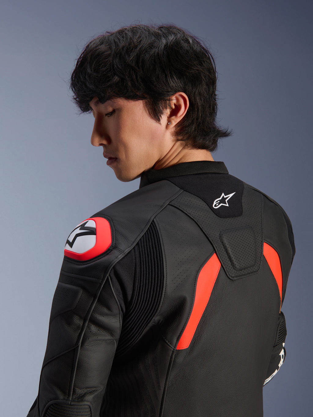 Chaqueta de cuero Alpinestars GP Plus R V4 Airflow, negra con detalles en rojo flúor y blanco, vista de cerca de la espalda y el hombro en un modelo, con zonas de cuero perforado, logotipo de Alpinestars y protección de hombro integrada para un alto rendimiento en motociclismo.