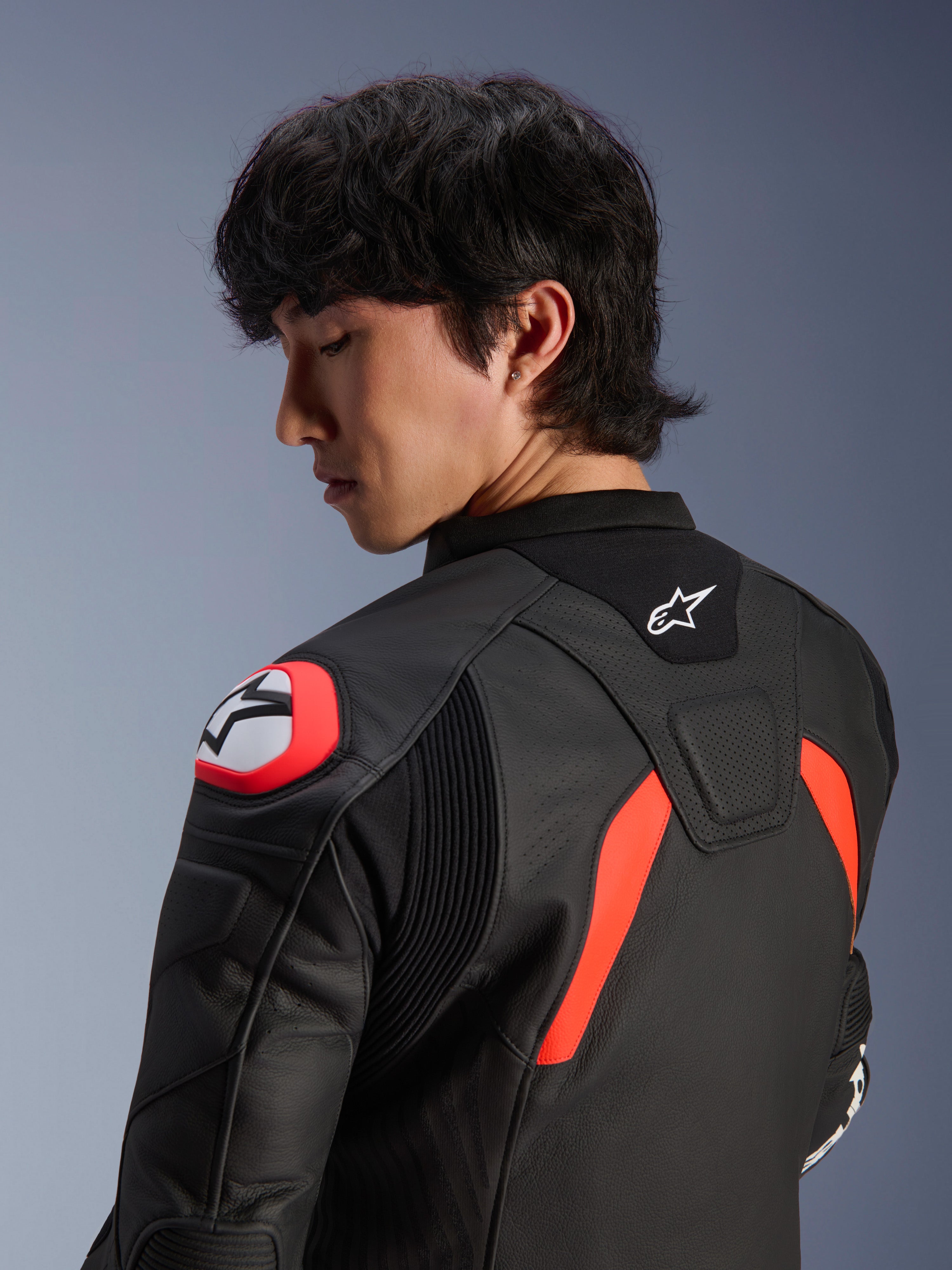 Chaqueta de cuero Alpinestars GP Plus R V4 Airflow, negra con detalles en rojo flúor y blanco, vista de cerca de la espalda y el hombro en un modelo, con zonas de cuero perforado, logotipo de Alpinestars y protección de hombro integrada para un alto rendimiento en motociclismo.