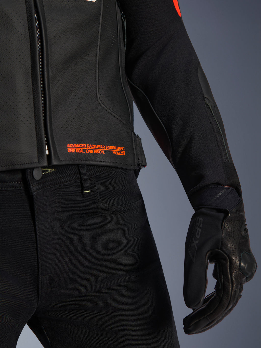 Chaqueta de cuero Alpinestars GP Plus R V4 Airflow, primer plano de la cintura y la manga, cuero perforado negro con texto en rojo flúor que dice 'Advanced Racewear Engineering', combinada con pantalones de moto negros y guante de moto SPX 7