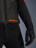 Chaqueta de cuero Alpinestars GP Plus R V4 Airflow, primer plano de la cintura y la manga, cuero perforado negro con texto en rojo flúor que dice 'Advanced Racewear Engineering', combinada con pantalones de moto negros y guante de moto SPX 7